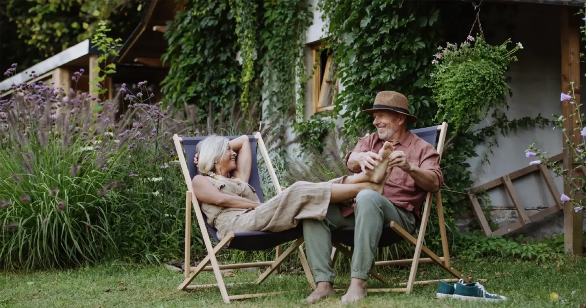 Una pareja de ancianos sentados en sillas de exterior en su patio trasero, disfrutando de un momento de paz.