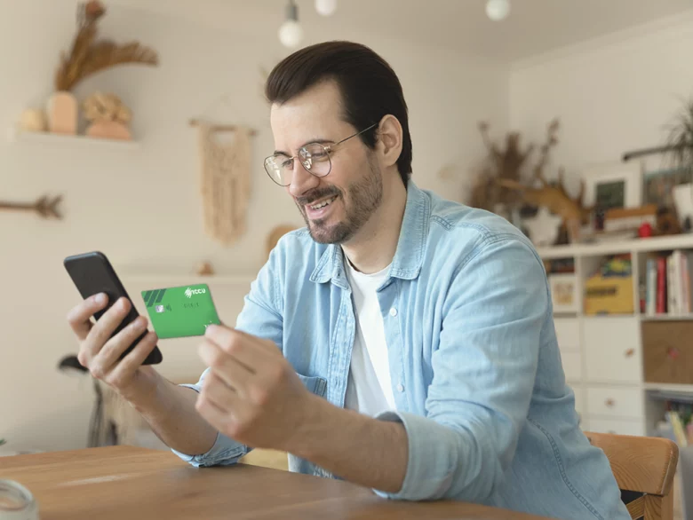 man looking at his phone and holing an ICCU debit card