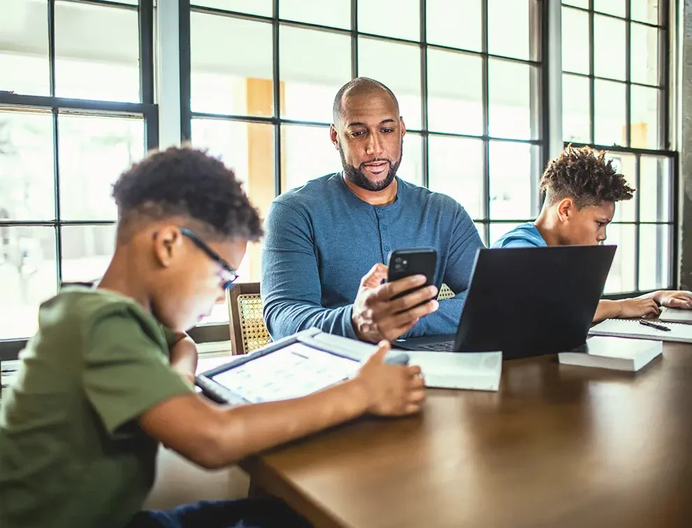 Parent and children using digital devices together at home, promoting cybersecurity awareness and safe online habits.