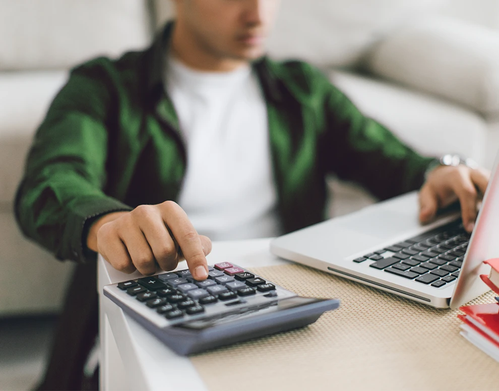 A man using a laptop and calculator, symbolizing smart financial planning and the benefits of ICCU’s High-yield Online Savings Account.