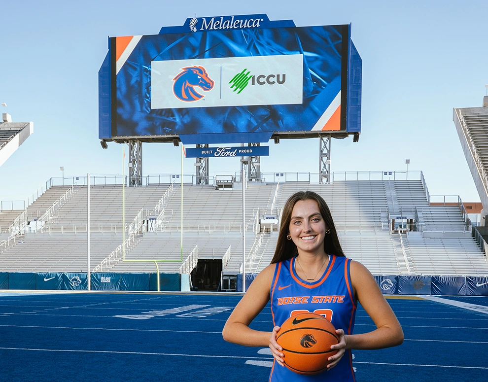 Natalie Pasco stands proudly holding a basketball in front of a jumbotron displaying the Boise State Broncos and ICCU logos.