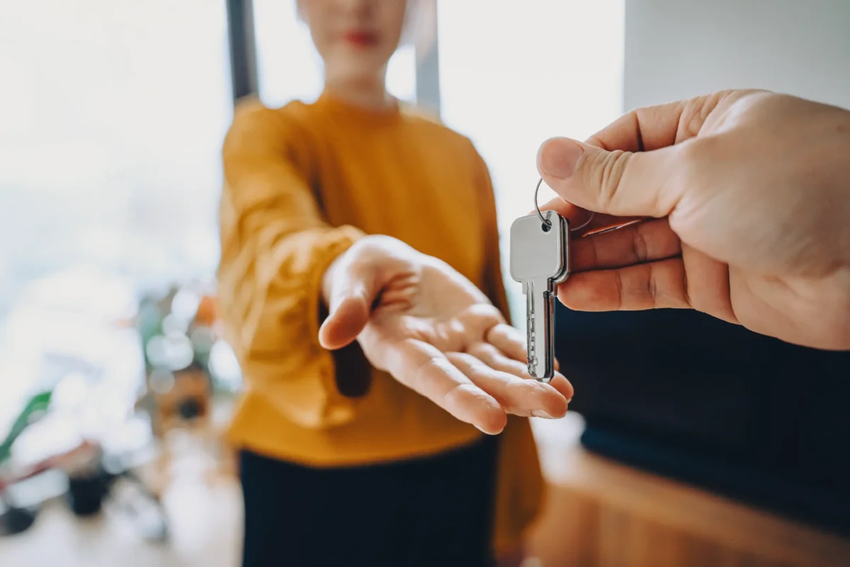 Someone hands a woman in a yellow sweater the keys to a house.
