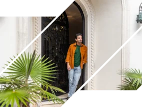 A wealthy man smiles outside an arched doorway with plants.