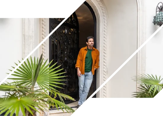 A wealthy man smiles outside an arched doorway with plants.