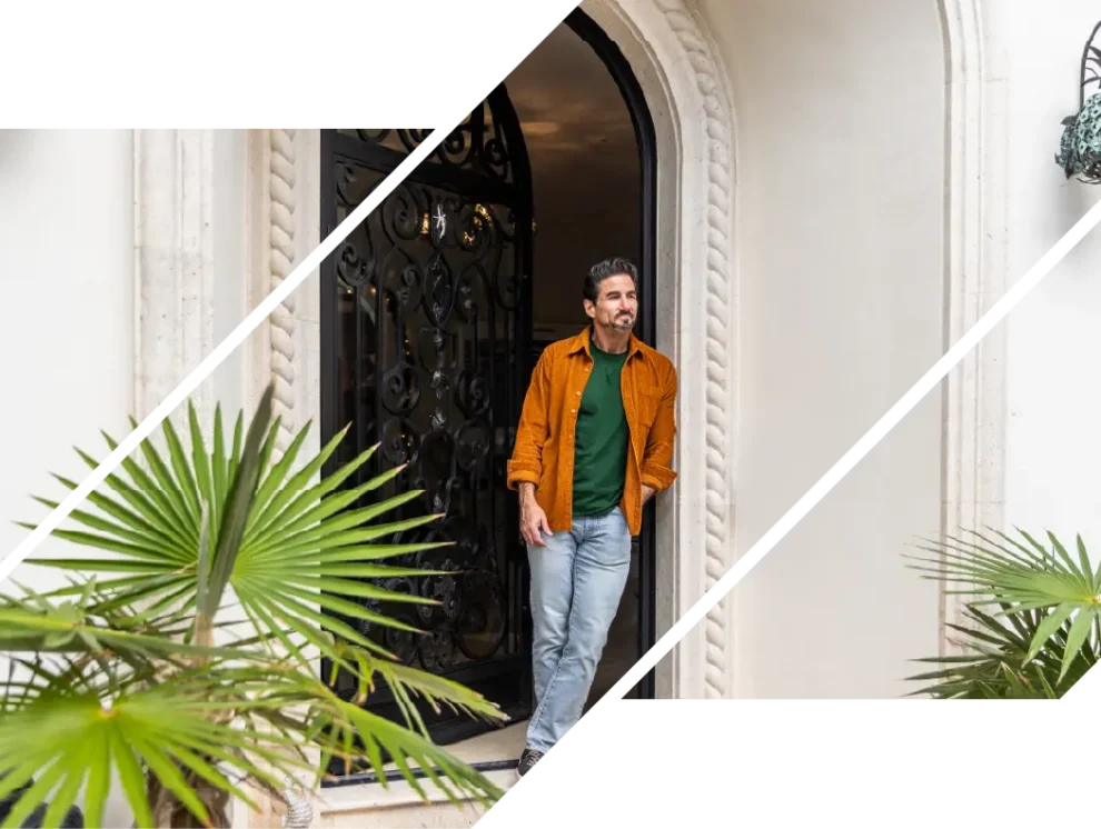 A wealthy man smiles outside an arched doorway with plants.
