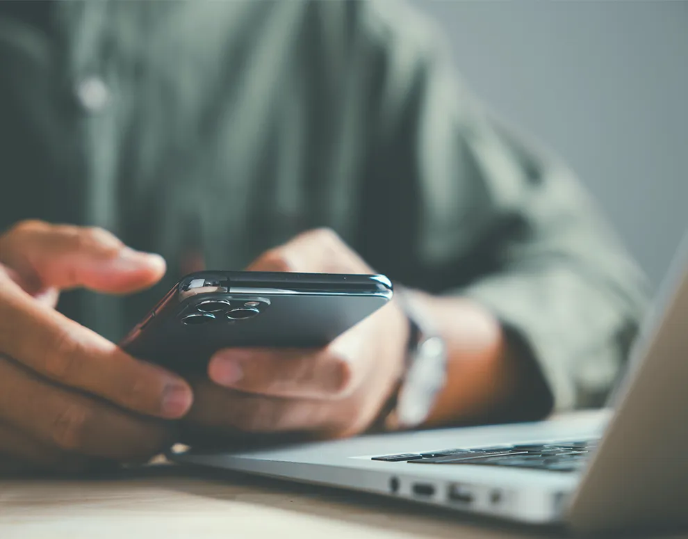 Individual using a smartphone beside a laptop, symbolizing multi factor authentication for secure eBranch sign in