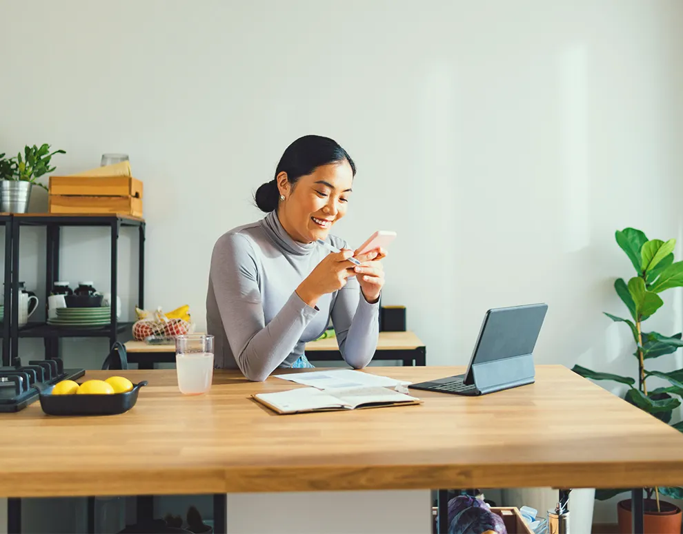 Persona que utiliza un smartphone en un espacio de trabajo doméstico, simbolizando la inscripción y la iniciación en las herramientas de banca online