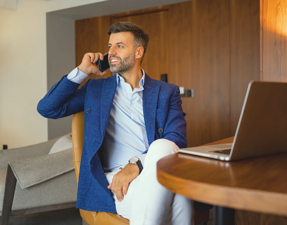 Person seated at a desk speaking on a smartphone with a laptop nearby, representing financial planning conversations