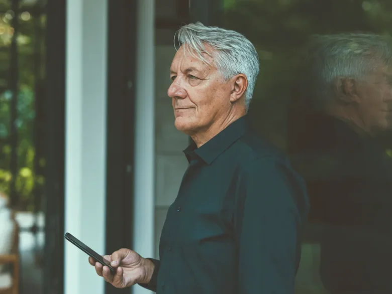Person using a smartphone near a window, reflecting retirement planning and long term financial confidence