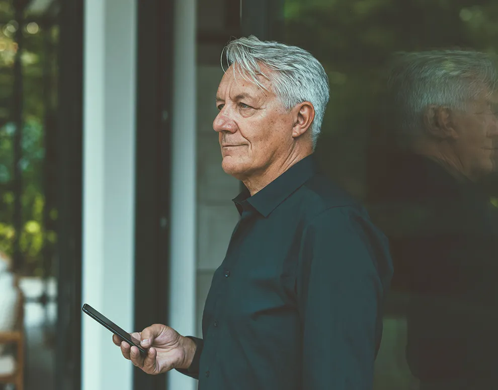 Person using a smartphone near a window, reflecting retirement planning and long term financial confidence