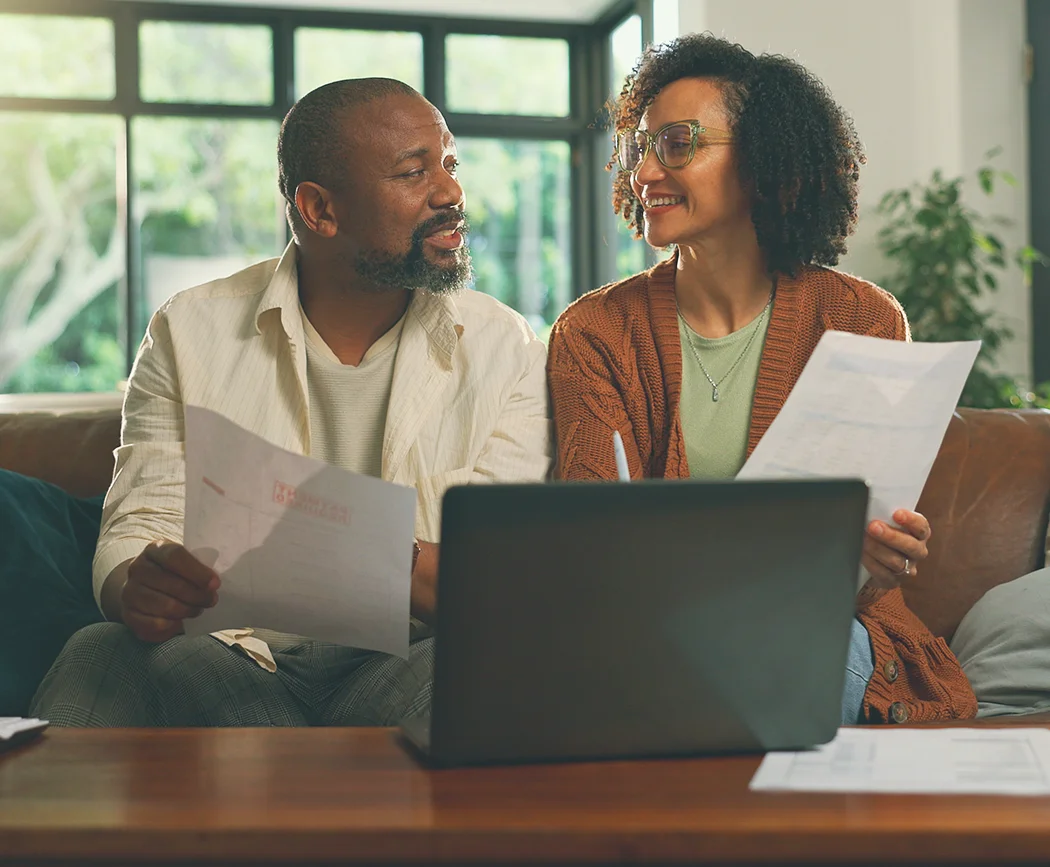 Couple reviewing loan documents and bills with laptop, planning payments and exploring Skip-A-Pay options online