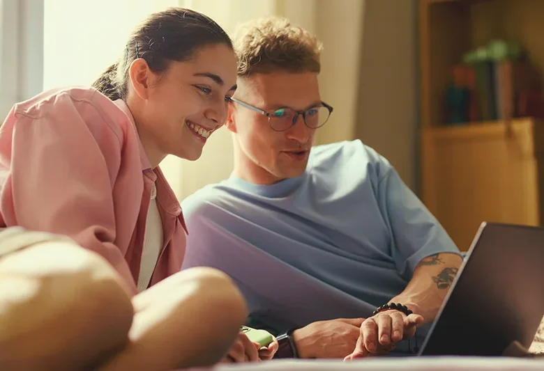 Two people reviewing finances and budgeting information on a laptop at home.