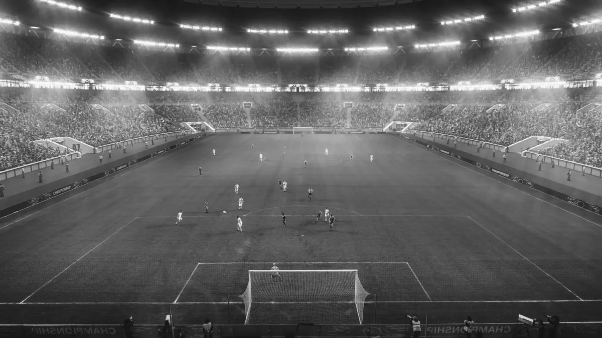 A grayscale image of a full football stadium during a game.